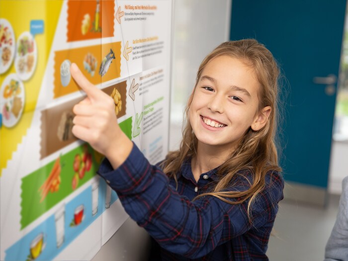 Eine Schülerin zeigt mit dem Finger auf ein Plakat, auf dem die Ernährungspyramide zu sehen ist.