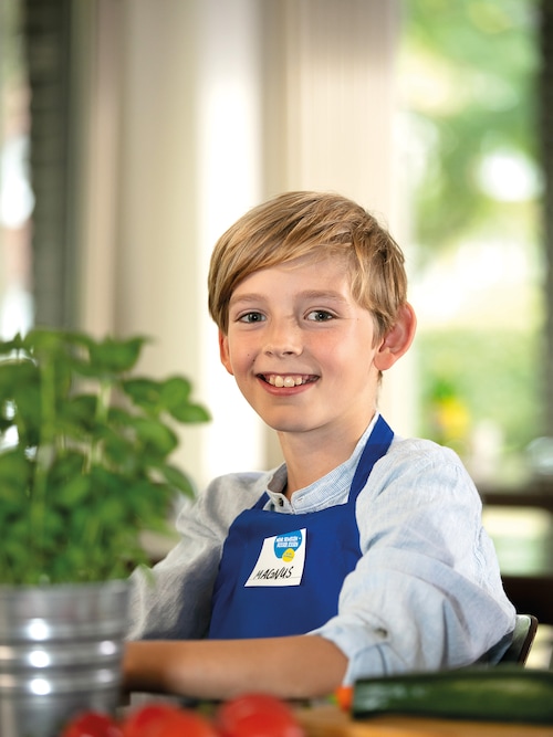 Ein Junge in einer blauen Schürze lächelt in die Kamera beim Projekttag 