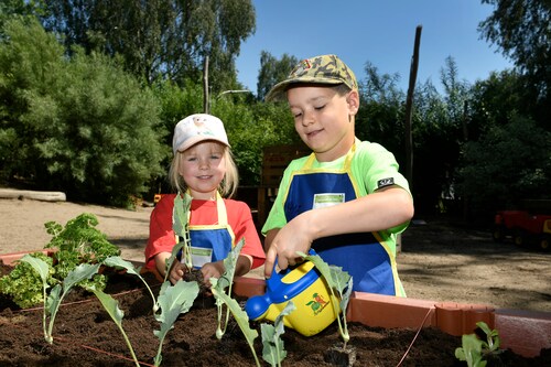 Zwei Kinder gießen die Setzlinge im Hochbeet bei der Anpflanz-Aktion Gemüsebeete für Kids von der EDEKA Stiftung