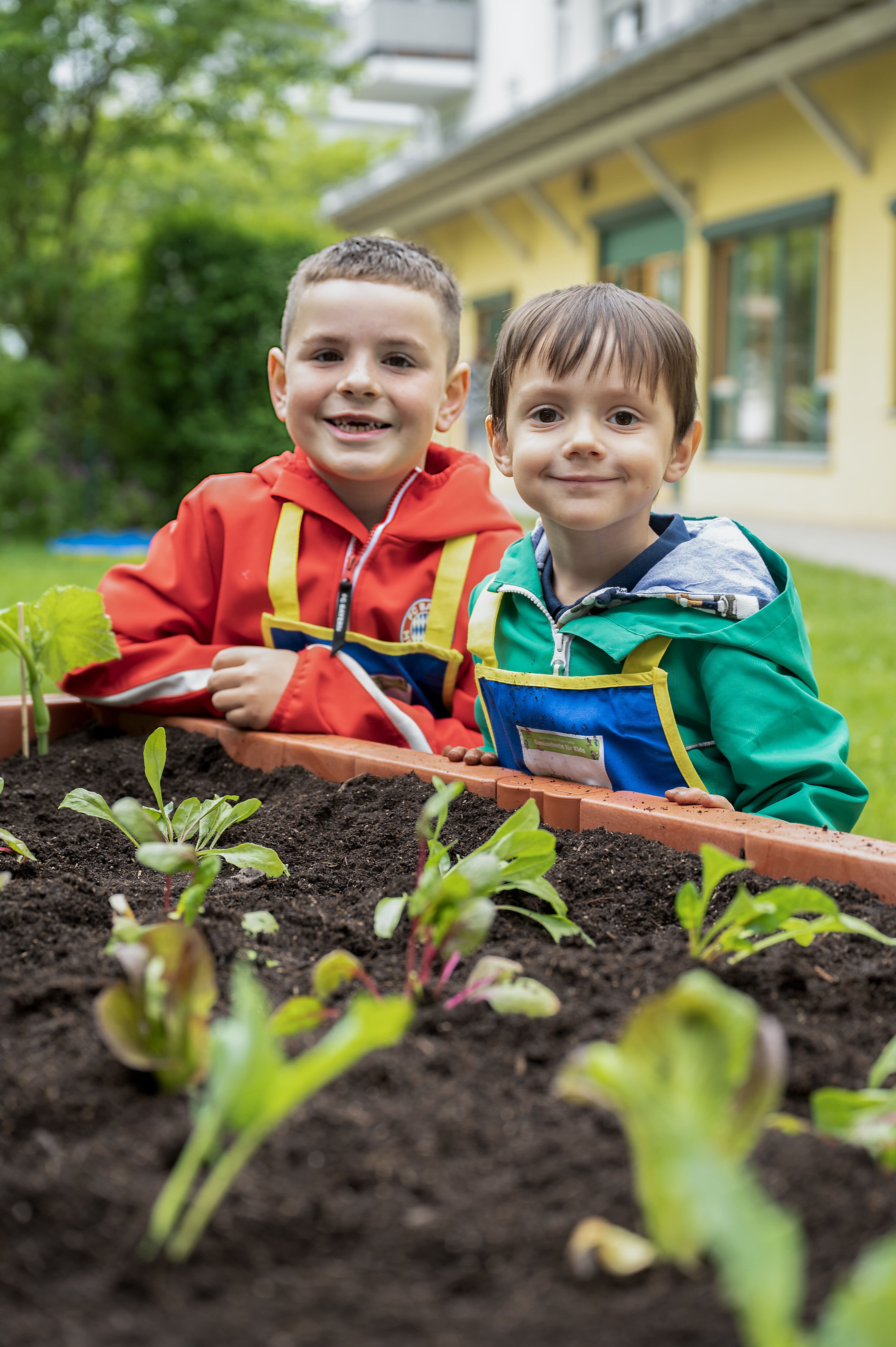Zwei Kita-Kinder stehen lächelnd an einem frisch bepflanzten Hochbeet bei "Gemüsebeete für Kids" der EDEKA Stiftung.