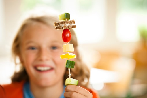Ein Junge hält lachend einen Paratenspieß in die Höhe, dies ist das aufgespiesste Frühstück am Projekttag.